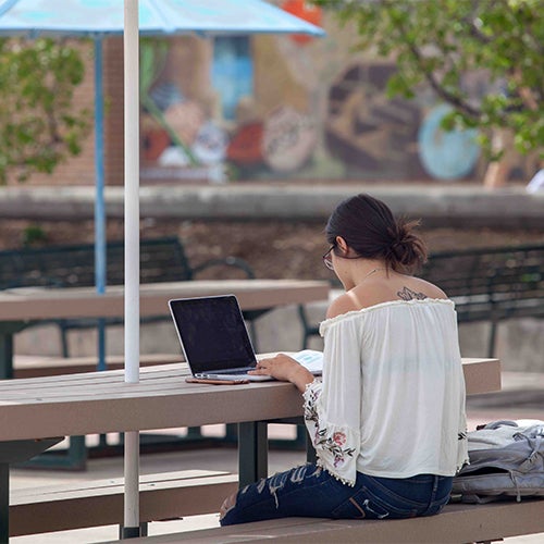 A student types during a beautiful day on the UCCS campus.